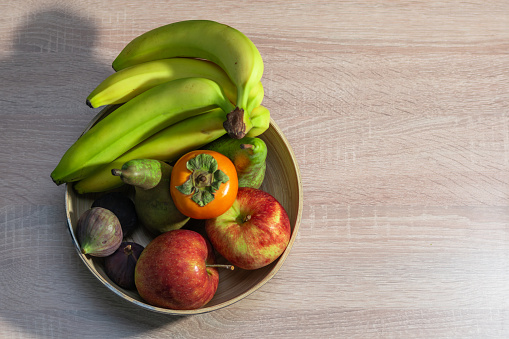 Top view of bowl containing pears apples and bananas on wood background