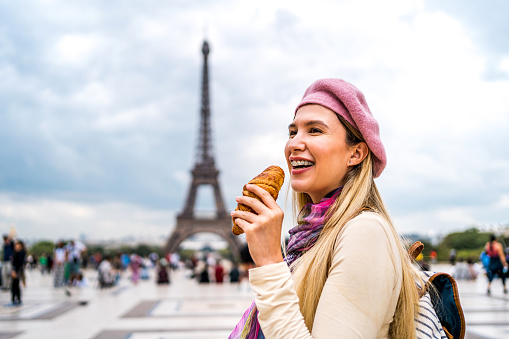 Cheerful woman eating croissant in front of the Eiffel Tower in Paris, France