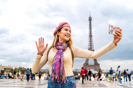Young happy woman tourist having a video call in front of the Eiffel Tower in Paris, France