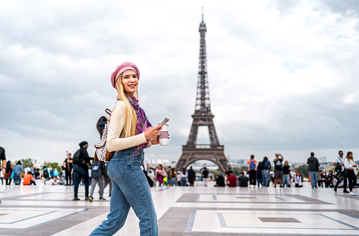 Young smiling woman tourist walking in front of the Eiffel Tower in Paris, France
