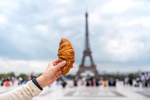 Woman's hand holding croissant in front of the Eiffel Tower in Paris, France