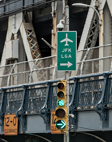 JFK and LGA sign on traffic light with manhattan bridge in the background (close up of directional signs to john f kennedy, laguardia airport) green light signal