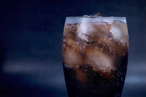 Cool glass of cola drink with ice, bubbles and fizz. Fresh cold sweet with ice cubes. Cola glass with summer refreshment on black.