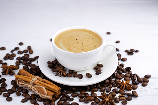 A cup of aromatic cappuccino and coffee beans on the white wooden table. Close-up. Selective focus.