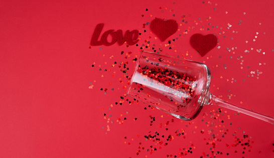 A two red hearts, word LOVE and small red hearts in wineglass on the red background. Valentine's Day concept. Banner. Top view. Copy space. Selective focus.