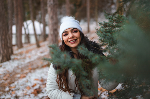 Portrait of a young woman in a forest during winter. She is wearing warm clothing.