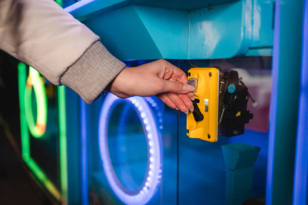istock Close-up of woman's hands inserting a coin into a claw machine arcade game 1937778565