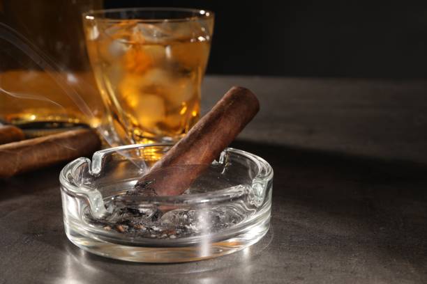 istock Smoldering cigar, ashtray and whiskey on grey table, closeup. Space for text 1937794194
