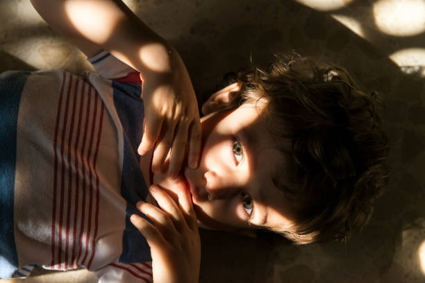 Creative portrait of a child with a pattern of lights and shadows on his face created to pass sunlight through a window.