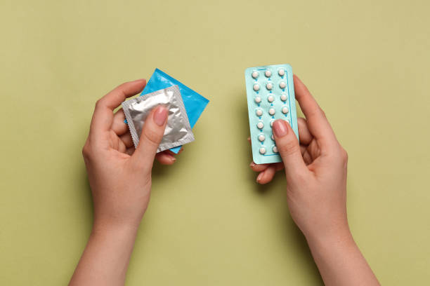 オリーブ色の背景にコンドームと避妊薬を持つ女性、上面図。避妊方法の選択 - group sex ストックフォトと画像