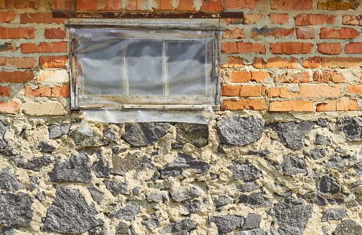 Window is covered with oilcloth. Wall of red brick and gray stone