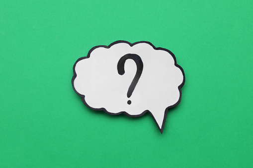 Paper speech bubble with question mark on green background, top view