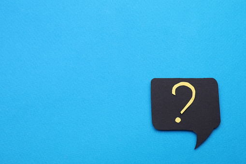 Paper speech bubble with question mark on light blue background, top view. Space for text