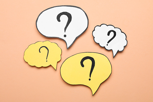 Paper speech bubbles with question marks on beige background, flat lay