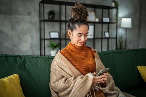 Portrait of cheerful woman using smart phone at home texting or surfing internet