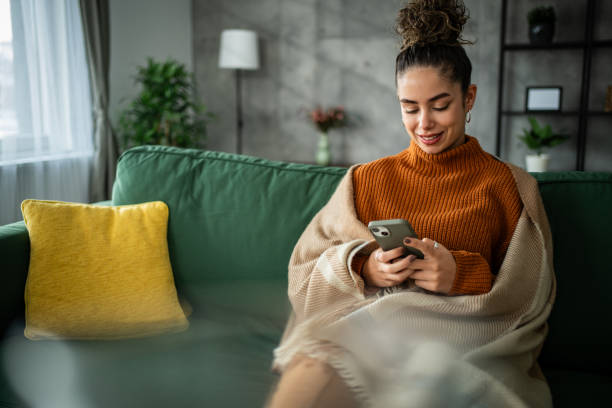 istock Happy white young woman sitting alone on sofa in living room and using technology for networking. 1937831384