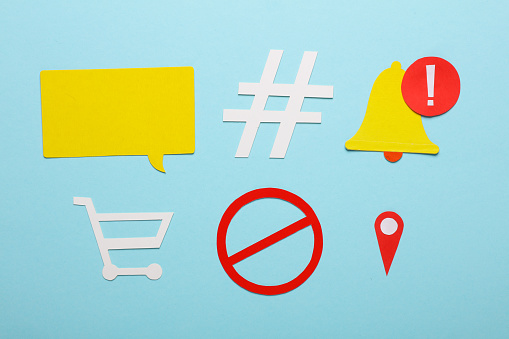 Paper cut speech bubble icons, prohibition sign, geolocation point, notification bell, hashtag, shopping cart on blue background