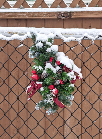 An abandoned wreath hangs on a chain-link fence in a residential neighbourhood in Surrey, British Columbia. Winter morning with snow in Metro Vancouver.