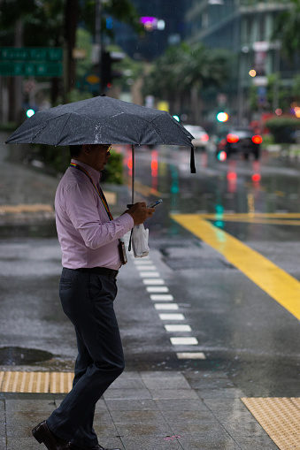A man walks through the afternoon rain showers in the central part of Singapore City, Singapore