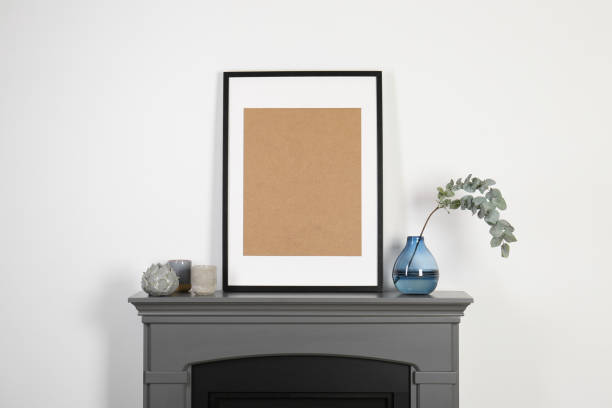 istock Empty frame, candles and eucalyptus branch in vase on fireplace near white wall indoors. Interior design 1937891140