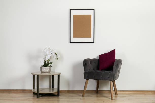 istock Comfortable armchair, cushion, table with orchid and picture frame indoors. Interior design 1937891146