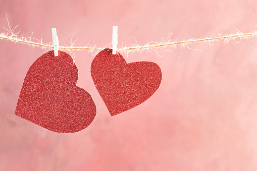 Two red hearts with clothespins on a gray rope on a pink background for Valentine's Day