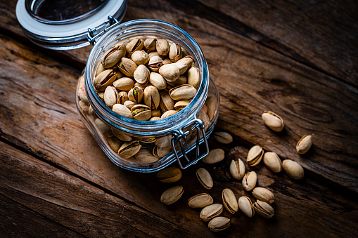 Fresh unshelled organic pistachios in an airtight glass jar shot on rustic wooden table. High resolution 42Mp studio digital capture taken with Sony A7rII and Sony FE 90mm f2.8 macro G OSS lens