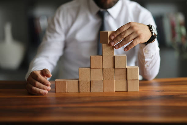 istock Businessman hand pulling out or placing wood block on the tower and semi-pyramid in modern office. Plan and strategy in business. 1937974947