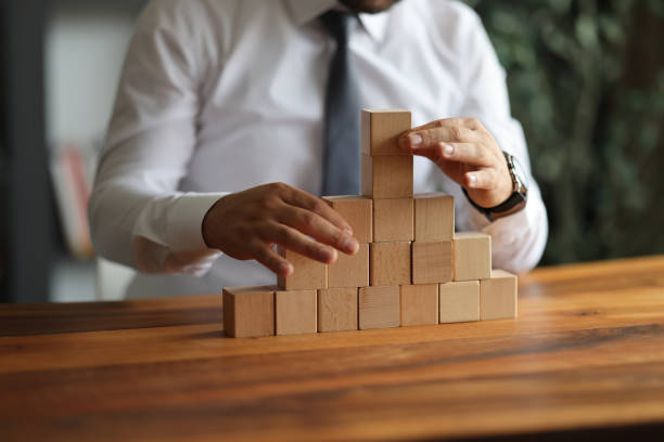 istock Businessman hand pulling out or placing wood block on the tower and semi-pyramid in modern office. Plan and strategy in business. 1937985521