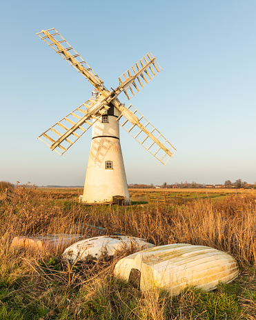 Thurne wind pump on a blue sky afternoon, upturned rowing boats in foreground - Norfolk. Thurne, Feb 2023