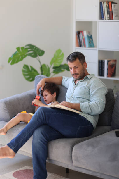istock Father is reading a book and son is playing games 1938003350