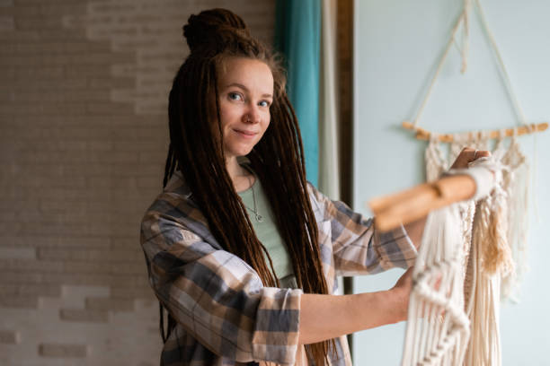 istock Young woman with dreadlocks weaves home decor from cotton thread macrame, looking at camera 1938005445