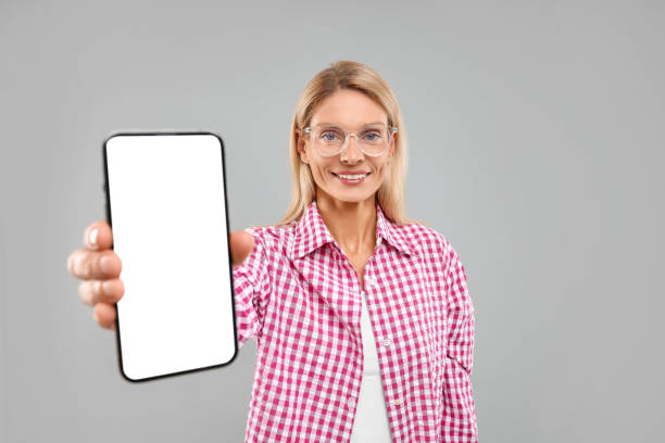 istock Happy woman holding smartphone with blank screen on grey background 1938007026