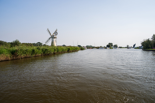 River Thurne and Thurne mill with a Norfolk Wherry sailing boat in the distance on the Norfolk Broads September, 2023