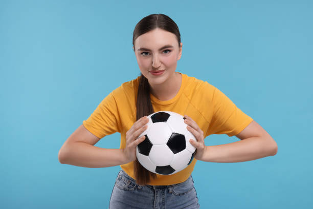 istock Beautiful soccer fan with ball on light blue background 1938024407