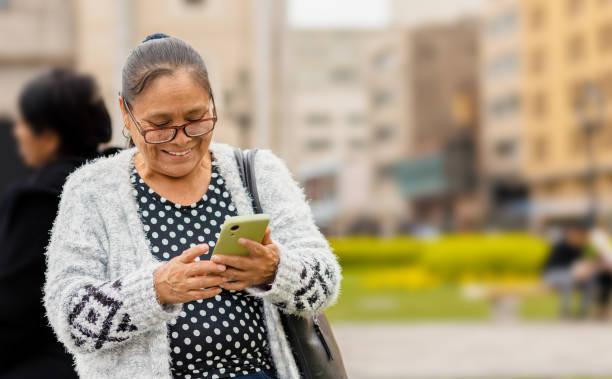 donna adulta latina, con un'espressione felice, in città usando il suo smartphone, inviando messaggi audio e digitando. spazio di copia. - main street audio foto e immagini stock