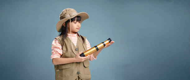 istock Little girl wearing camping clothes, holding binoculars for studying. 1938077519
