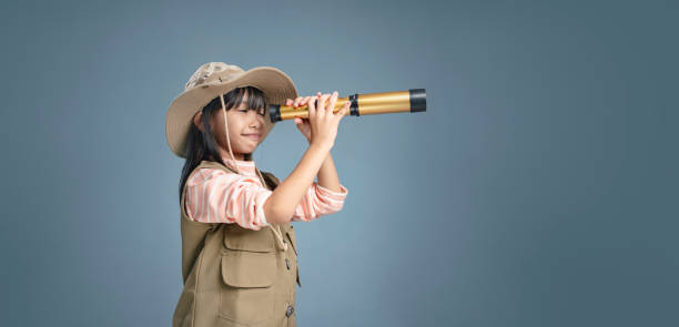istock Little girl wearing camping clothes, holding binoculars for studying. 1938079722
