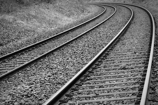 Low angle black and white view of railway lines curving around a corner in the distance