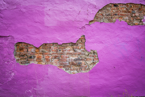 Horizontal purple paint peeling to expose an old brick wall underneath.