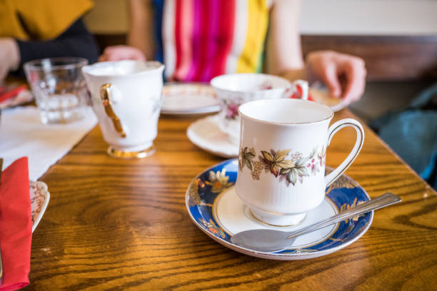 A white and blue china teacup set with a spoon on a wood coffee table with two people sitting in the background.