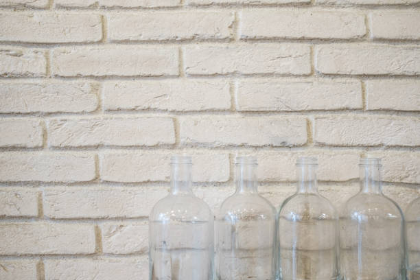 Four empty glass bottles lined up at the bottom of a white painted brick wall.