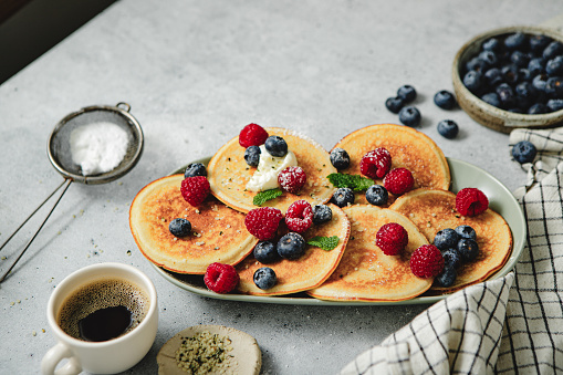 Pancakes stack with different berries and black coffee on kitchen table, Freshly prepared breakfast served on table.