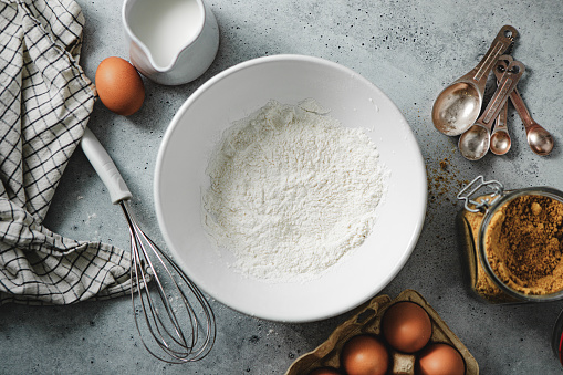 Top view of flour in a mixing bowl with a wire whisk and eggs on wooden kitchen table. Preparing pancake in kitchen at home.