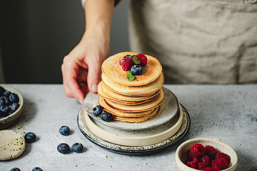 Close-up of woman hand serving pancakes with berries on a plate