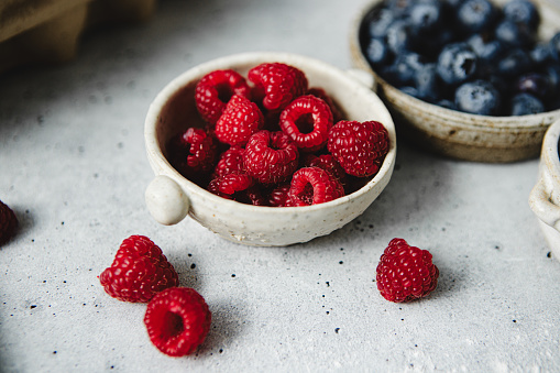 Close-up of fresh berry fruits in bowls on a kitchen counter. Juicy raspberries and blueberries in bowls on counter.