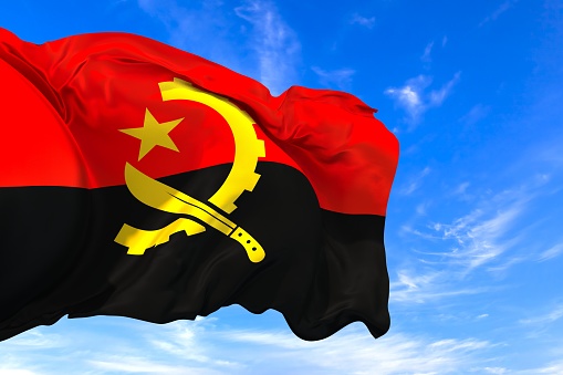 The national flag of Angola with fabric texture waving in the wind on a blue sky. 3D Illustration