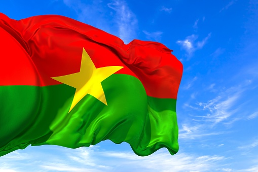 The national flag of Burkina Faso with fabric texture waving in the wind on a blue sky. 3D Illustration