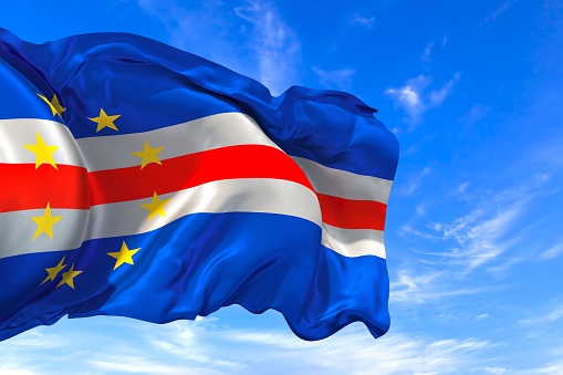 The national flag of Cape Verde with fabric texture waving in the wind on a blue sky. 3D Illustration