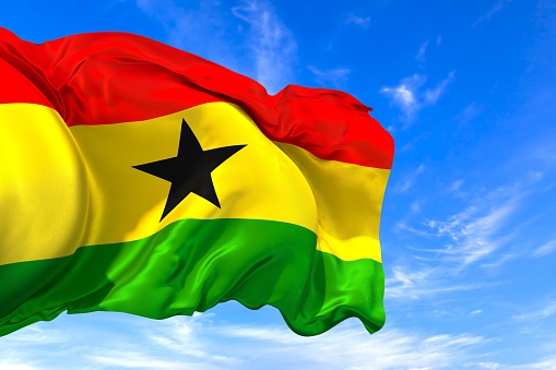 The national flag of Ghana with fabric texture waving in the wind on a blue sky. 3D Illustration